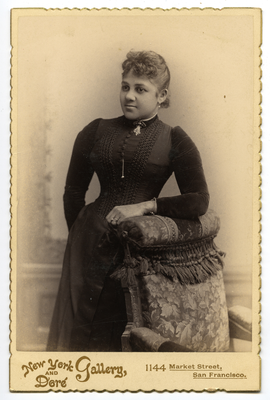 Portrait of woman in black dress leaning on chair