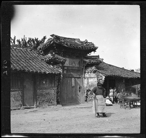Old woman standing outside the entrance to an ancient house in China, ca.1900