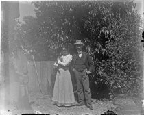 Woman holding cat, man wearing fedora in garden, c. 1912