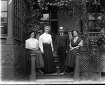 Three women, one man on steps of brick building, c. 1912