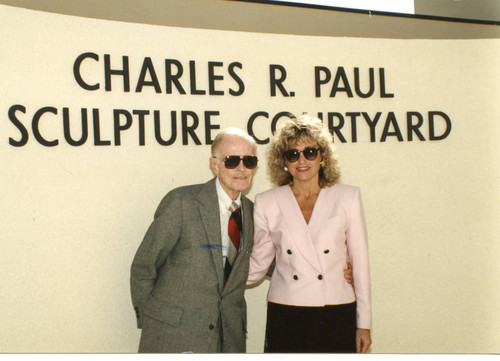 Charles R. Paul and Claudia Arnold standing in front of the sign "Charles R. Paul Sculpture Courtyard"