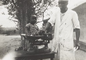 Male nurse weighing baby, Nigeria, ca. 1936
