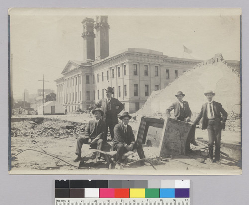 [Men posing beside safe in ruined lot near Mission and Mary Sts. U.S. Mint in background.]