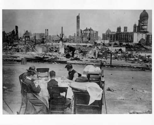 [Group of refugees sitting down to eat a meal amidst the ruins of the city]