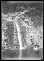 Two men on rocks at foot of waterfall