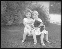 Twins in yard, sitting on stool, holding puppies