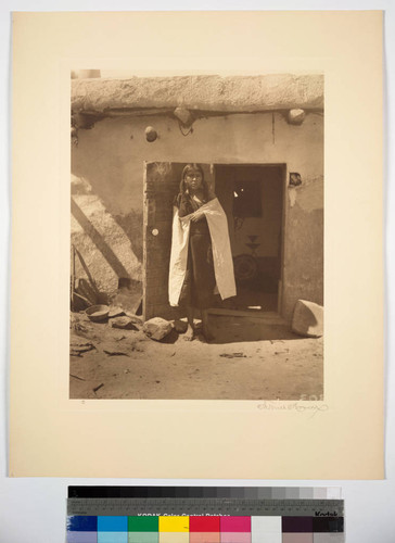 A young Hopi woman standing in doorway of adobe building