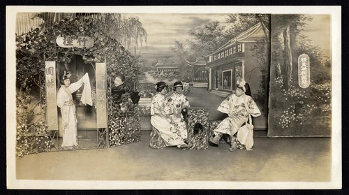Man talks with two seated women while a standing woman and a maid look on and talk /