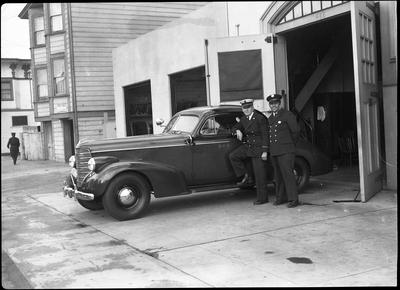 Two firemen standing next to car in front of garage