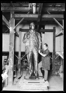 Man creating a bronze statue of a man in a factory