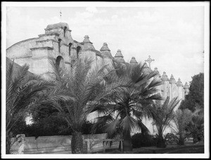 South front of Mission San Gabriel with palm trees, ca.1900