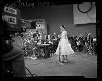Dorothy Lamour standing at microphone as Bing Crosby and Bob Hope watch at telethon for 1952 Olympic Games
