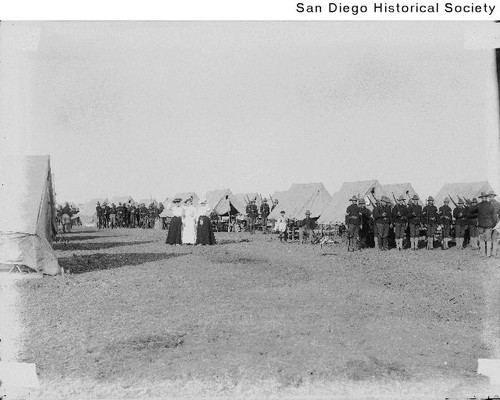 Three women standing near a group of soldiers at a military camp in Coronado