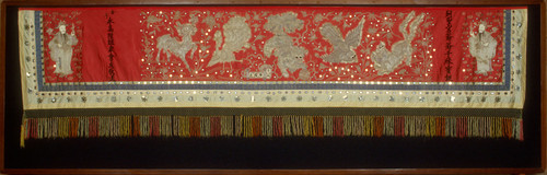 Banner, red background, fur in the design deer, peacocks, Buddha lion & flaming pearl, figures 7 black characters. 12' x3'. c. 1909