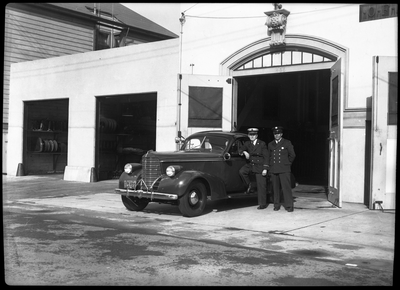 Two firemen standing next to car in front of garage