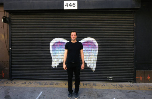 Unidentified man in a black T-shirt posing in front of a mural depicting angel wings