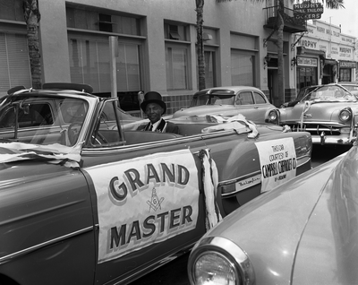 Mason with top hat sitting in backseat of convertible automobile with Grand Master banner