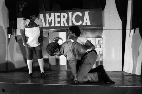 Performance: two men and a woman in a scene with the word "America" on the backdrop