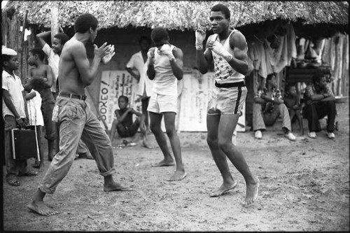 Three men boxing outdoor in front of a crowd, San Basilio de Palenque, 1975