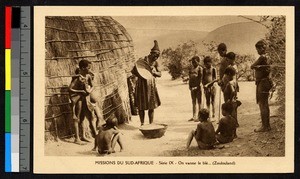 Woman pouring grain between baskets while children look on, South Africa, ca.1920-1940