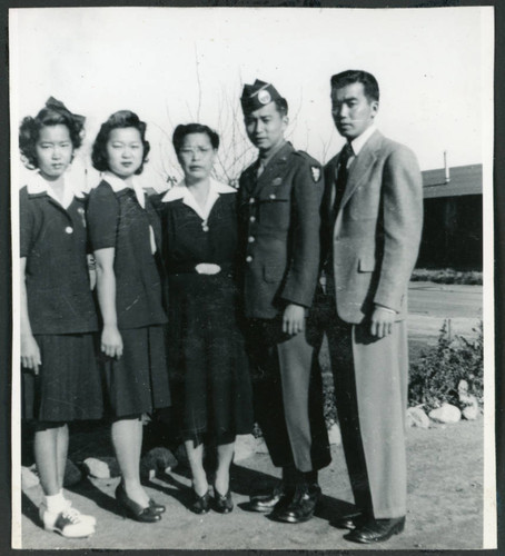 Photograph of five people, including an army soldier, posing in front of the Manzanar barracks