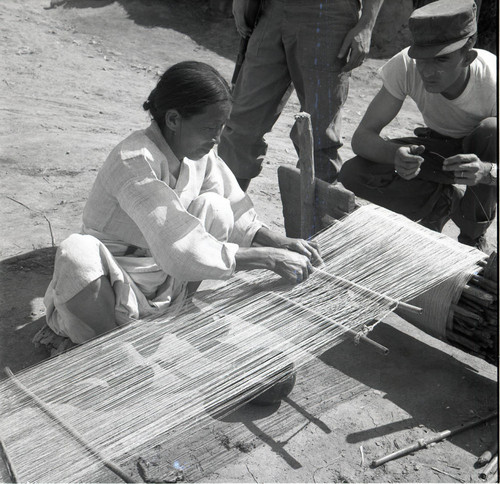 Soldier adming a woman weaving at a loom