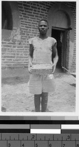 Man holding a clay brick outside of a building, Africa, August 1948