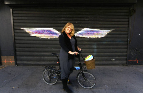 Unidentified woman posing on her bicycle in front of a mural depicting angel wings