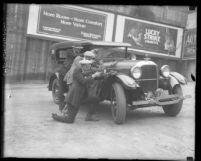 Three Los Angeles plain-clothed police men crouched behind car aiming their guns, circa 1925