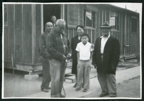 Photograph of people in front of a barracks at Manzanar