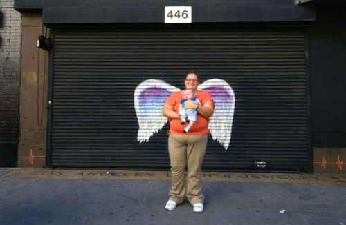 Unidentified woman and a baby posing in front of a mural depicting angel wings