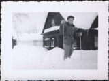 Boy posing on skiis outside of snow-covered cabin