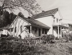 Unidentified two-story home with a second-story porch and an attached, one-story wing, located below a low, Douglas-fir covered hill, 1960s or 1970s