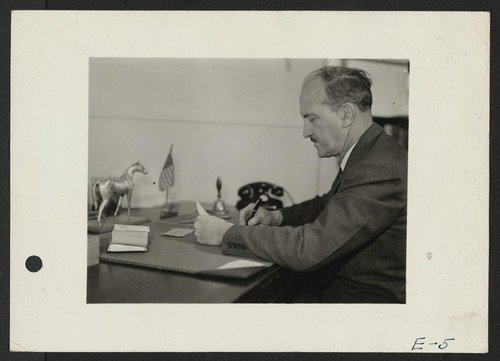 Charles F. Ernst, Project Director, at his desk in the Administration building at the Topaz Relocation Center. Photographer: Parker, Tom Topaz, Utah