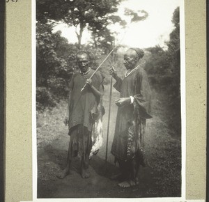 Two Bali men with spears and wild-cat skins. In the skins they carry their pipes, tobacco and drinking horn. The ivory bracelet worn by one of them is a mark of status