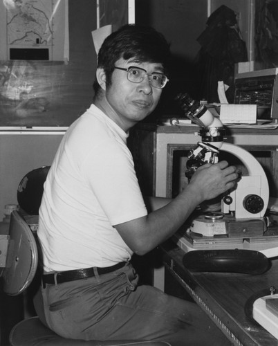 Chemist Toshio Ishizuka using a microscope in the core laboratory aboard the D/V Glomar Challenger (ship) during the Deep Sea Drilling Project. 1983