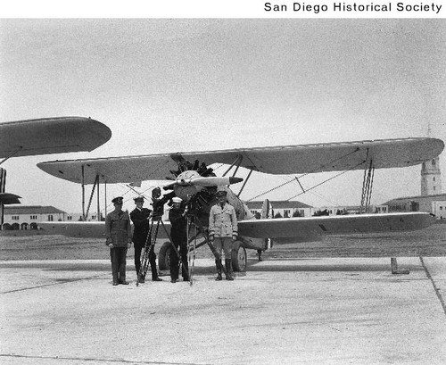Four men standing with a camera in front of a biplane
