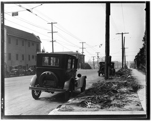 Early style automobiles parked on the side of a paved road