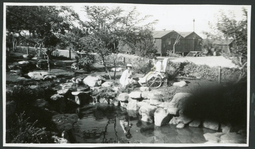 Photograph of Peter Hondo in a wheelchair with Thelma McBride standing next to him near a pond in Manzanar