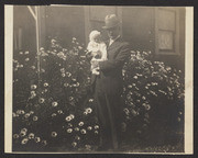 E. E. Wood and baby in front of flowering shrub