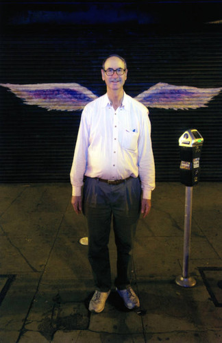 Unidentified man in white shirt posing in front of a mural depicting angel wings