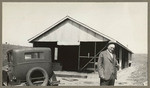 [Alfred Fuhrman standing near parked car and shed]