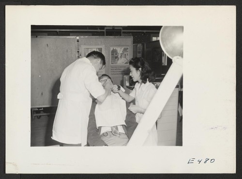A Japanese-American dentist and his assistant work on a resident with makeshift equipment and clinic arrangements. Photographer: Parker, Tom Amache, Colorado
