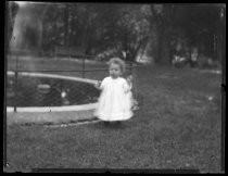 Toddler in dress on lawn near small pond