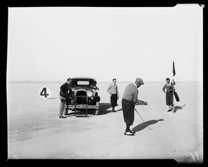 Group of men setting up a shot on a golf course near an automobile