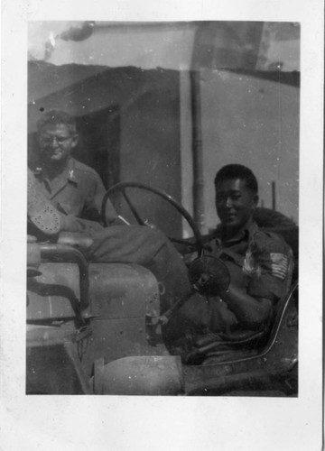 [Two men in military uniform with military vehicle]