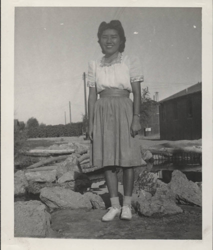 Young woman in front of pond, barracks and telephone poles at Poston incarceration camp