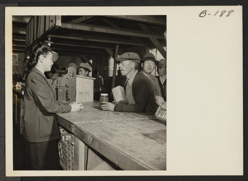 An elderly evacuee purchases peanut butter for a between meal snack. All meals for the residents are served in mess halls, and are merely supplemented by tid bits which the evacuees prepare in their own barracks. Photographer: Stewart, Francis Manzanar, California