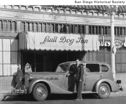 A man standing in front of a Packard automobile parked in front of the Bull Dog Inn