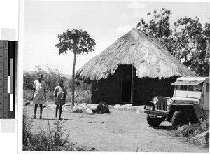 Two boys standing near a hut and jeep, Africa, November 1950